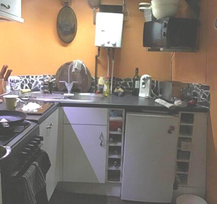 Compact kitchen corner with orange walls, dark countertops, gas stove, microwave, and open shelving.