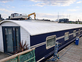 Blue and white houseboat docked with machinery on its roof