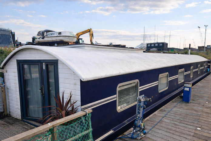 Long blue and white canal boat with a small boat and excavator on roof.