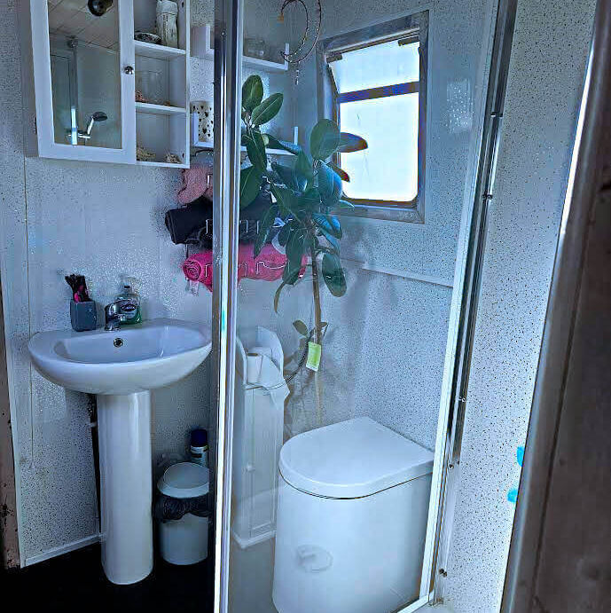 Small white bathroom with a pedestal sink, mirrored cabinet, composting toilet, and shower cabin.