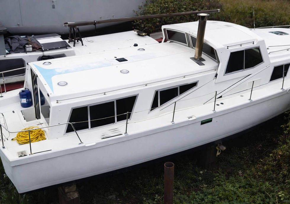 White houseboat docked on land next to another boat, with blue gas can and yellow rope on deck.