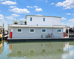Kenrose a modern grey and white houseboat moored in a calm harbor under a blue sky.