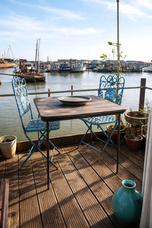 Deck with table and chairs overlooking a sunny boat harbor.