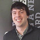 A headshot of Dominic Manterfield showing him smiling in front of a black background