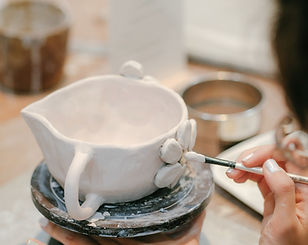 a woman is painting a white vase on a ta