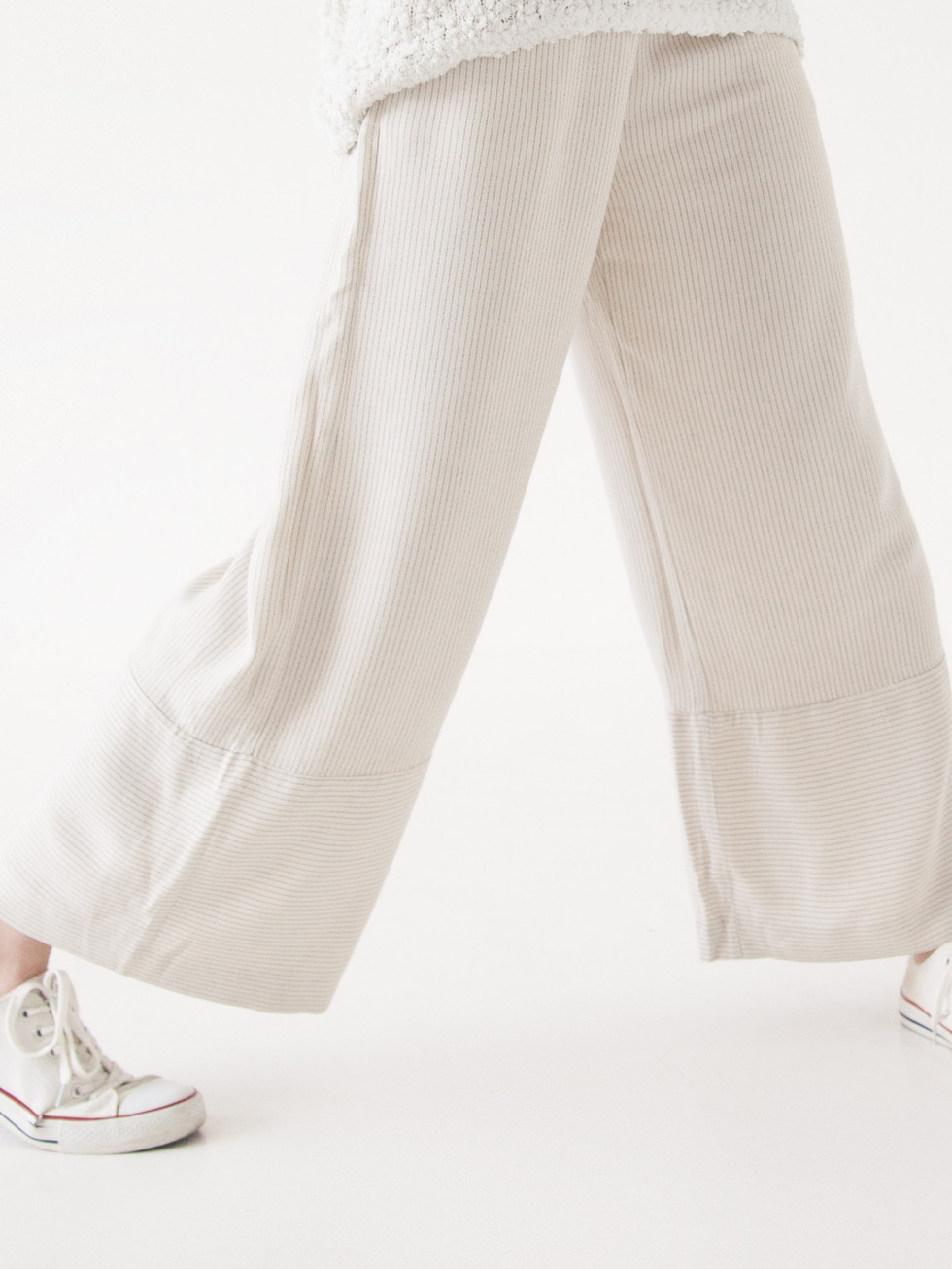 Person walking in beige Cotton Pants with white sneakers on white background.