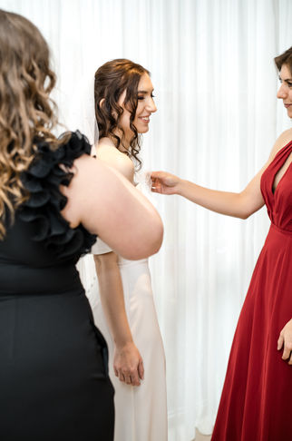 Bridesmaids adjusting the bride's dress, smiling, as she gets ready for wedding.