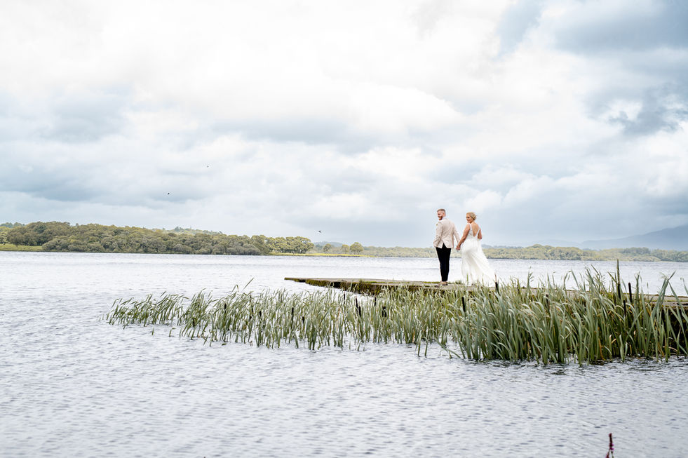 Bride and groom holding hands, standing on a dock by lake. Cork wedding.