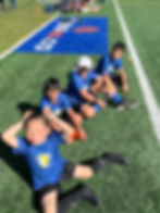 A group of children sit on the grass at the Kanata Montessori Soccer Jamboree 2023