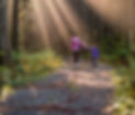 Sun rays beating down on mother and daughter walking in forest