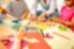 Foto de uma mesa redonda, com papéis e lápis coloridos. Em volta da mesa vemos crianças e uma professora utilizando essa brincadeira lúdica para desenvolver as habilidades das crianças. A foto ilustra o artigo Educação Lúdica para o site do Instituto Lapin.