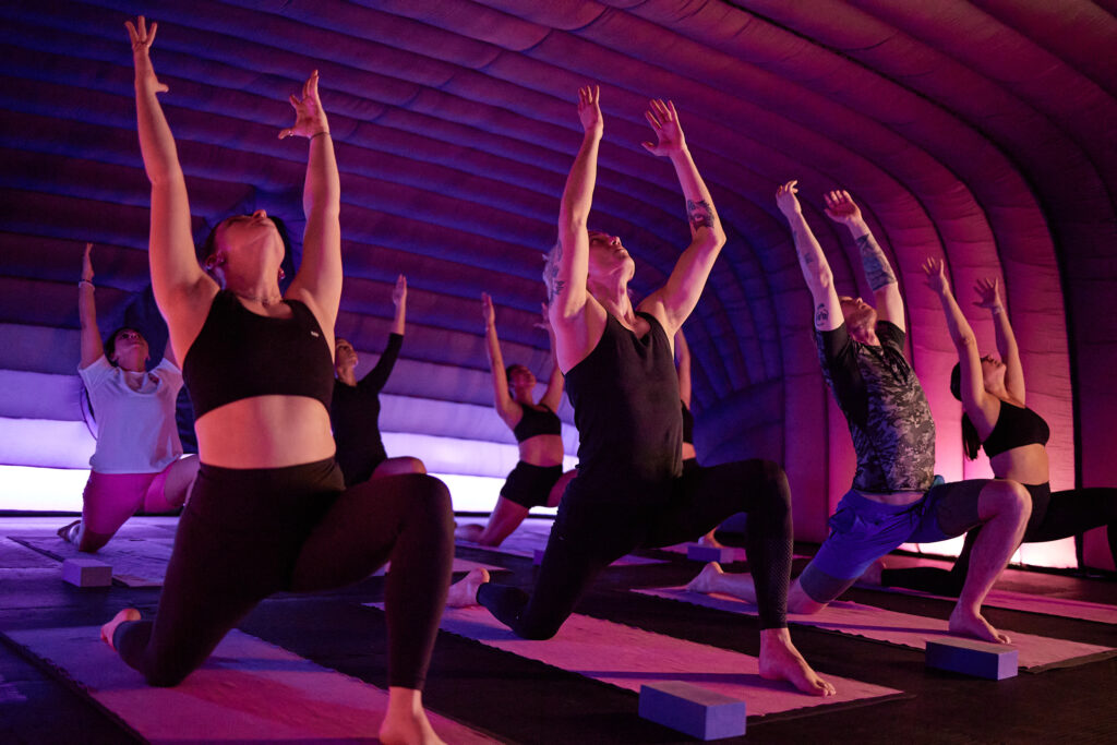 A class inside a Hotpod Yoga pod, lit in a purple glow