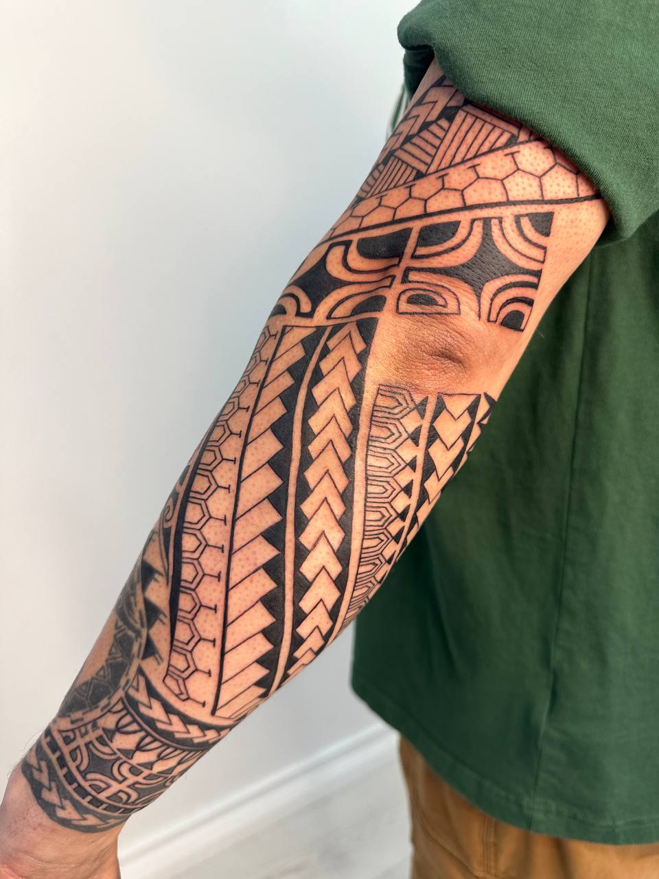 Bold black geometric forearm tattoo sleeve composed of repeated bands, chevrons, arcs, and honeycomb-like motifs