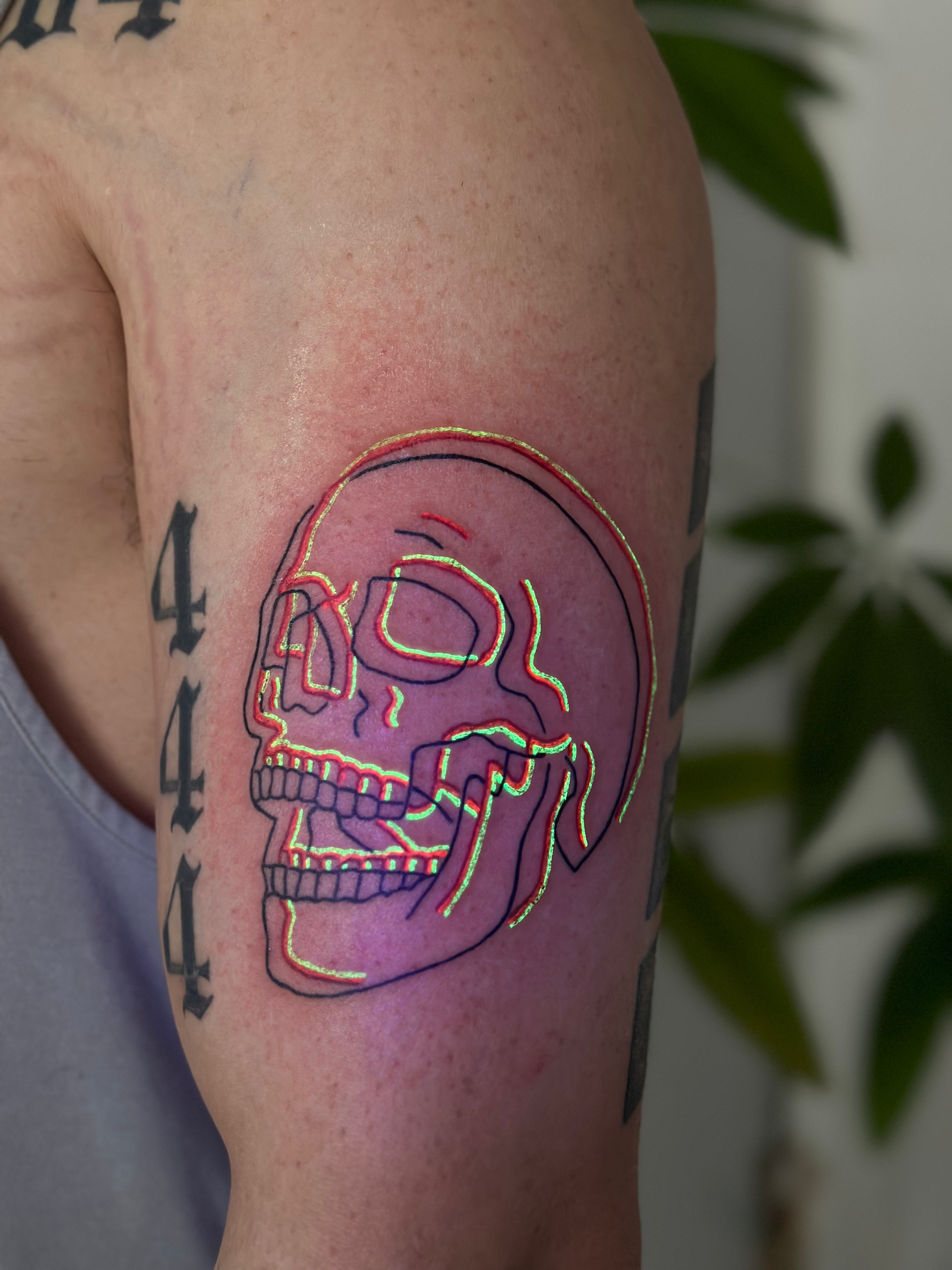 Upper-arm tattoo of a skull outlined with overlapping black, red, and fluorescent lime-green lines
