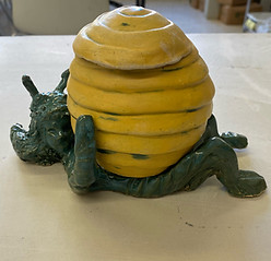 Ceramic piece that looks like a honey pot on top of a green figure.