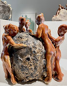 Ceramic piece of four orange figures leaning over a grey stone