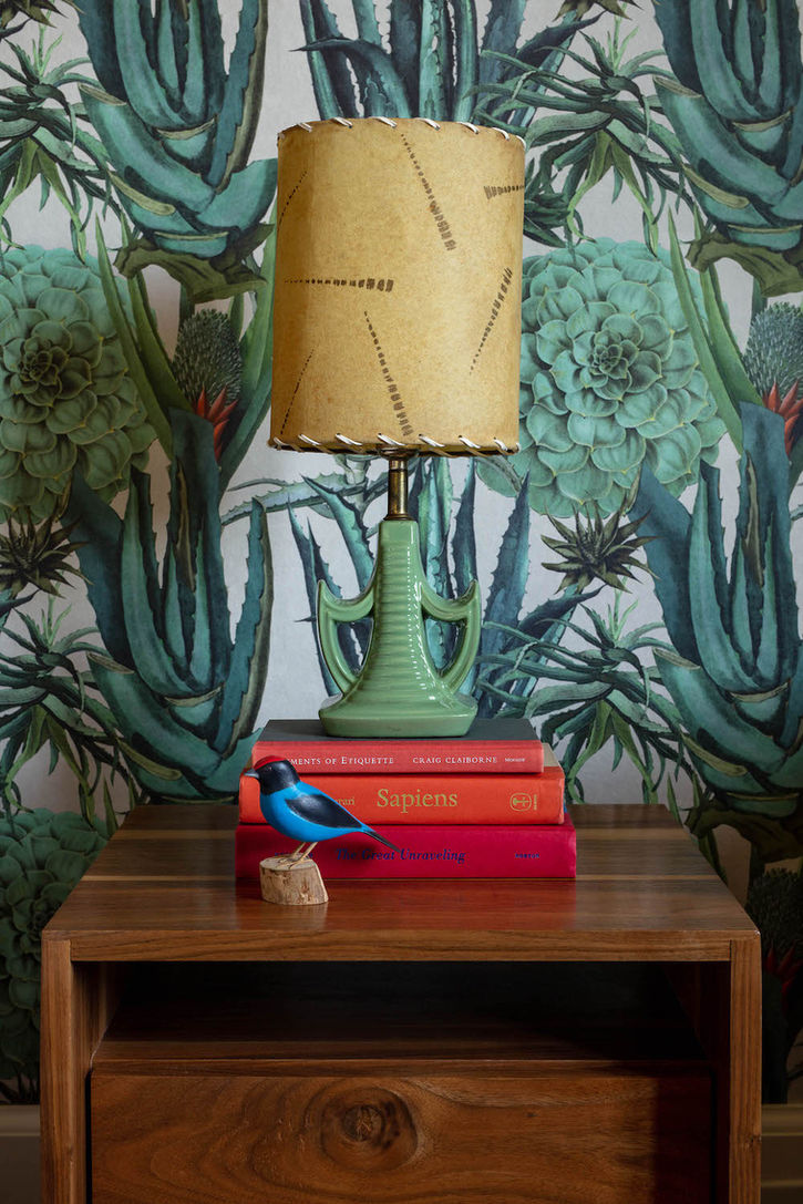 Close-up of bedside table adorned with red and orange books against leafy wallpaper backdrop - The Feel Interior Design, Los Angeles