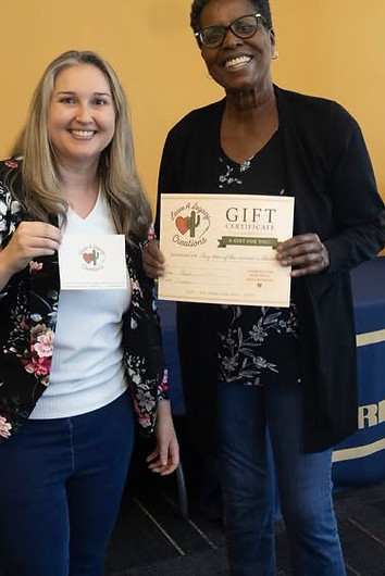Two women holding a recognition certificate and award card at a community event.