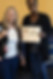 Two women holding a recognition certificate and award card at a community event.