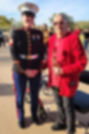 Woman Marine in dress uniform standing with an older woman holding a red rose during a community recognition ceremony.