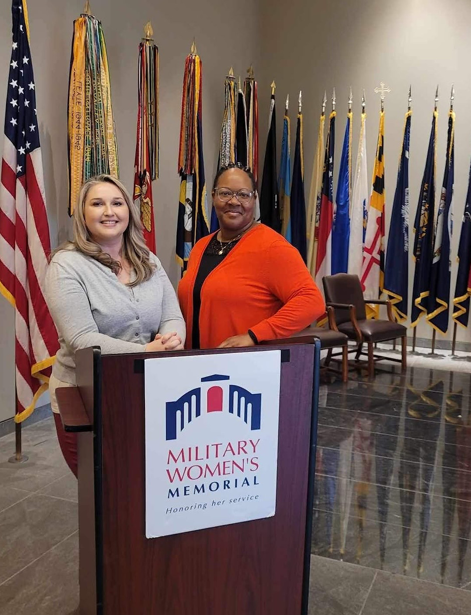 Two women standing at the Military Women’s Memorial podium with United States military flags displayed behind them.