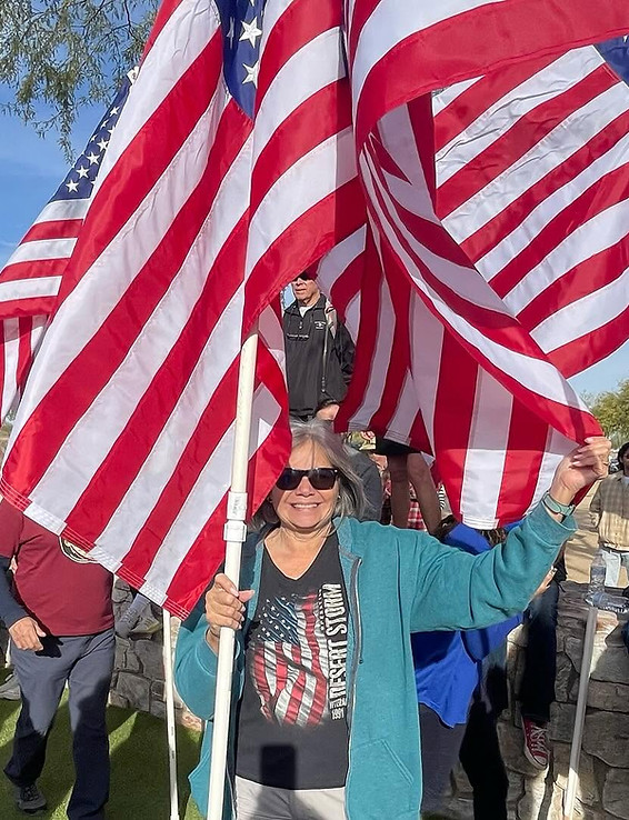 Woman veteran smiling while holding American flags at an outdoor community event.