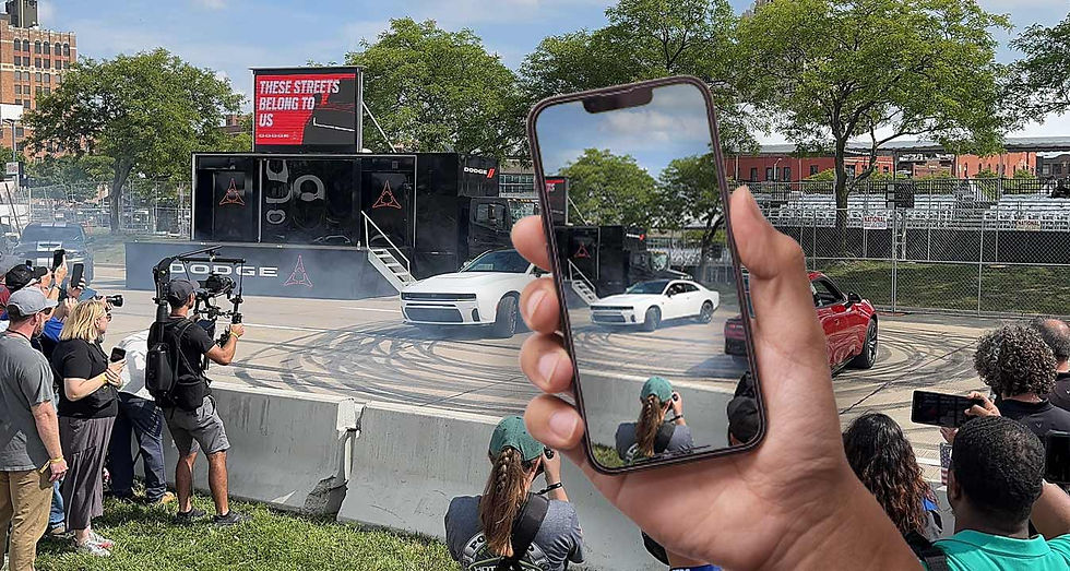 First-person view of an attendee filming Dodge Hellcats performing donuts on an iPhone.