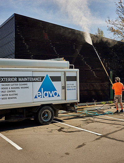 Technician washing a commercial building wall with an extension pole beside the Elavo truck