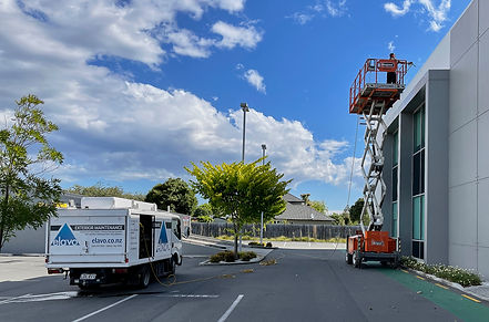 Elavo truck parked beside a commercial building while a worker on a scissor lift washes the upper wall