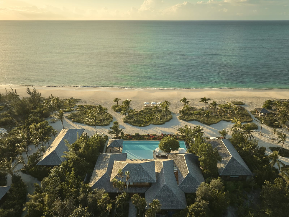 Aerial view of a beachfront resort with a pool, palm trees, and empty sandy beach beside a calm golden ocean at sunset.