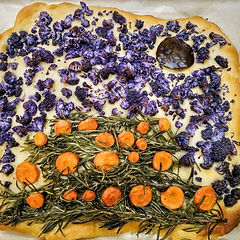 Colorful focaccia bread decorated to resemble a pumpkin patch landscape. Topped with vibrant purple cauliflower, rosemary sprigs, and orange carrot slices.
