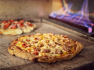 Two pepperoni pizzas baking in a stone oven, with flames visible on the side. The crusts are golden, conveying warmth and deliciousness.