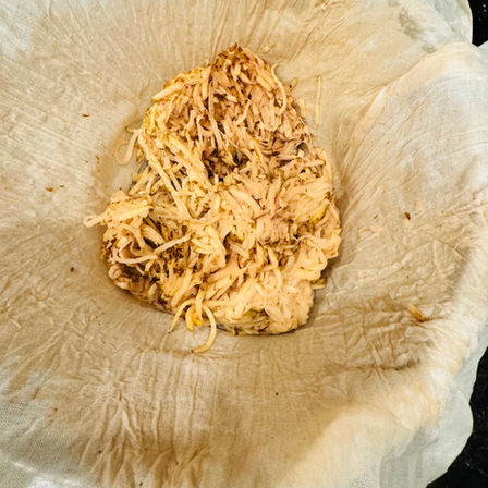 Grated potatoes sit on a piece of cheesecloth, ready for straining. The setting is a kitchen counter, with spice jars in the background.
