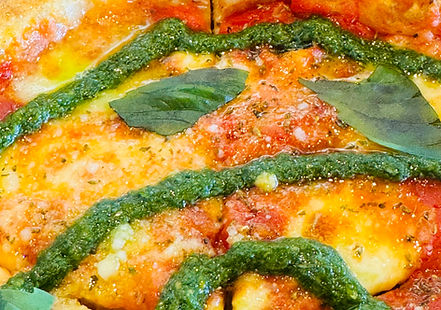 Shamrock pesto swirled on pizza creating a bright green herb sauce pattern over melted cheese and fresh toppings.