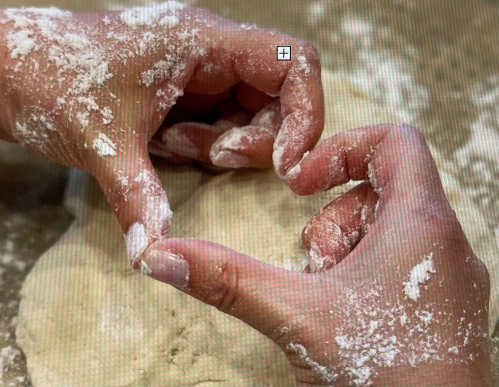Hands covered in flour shape dough into a heart on a light, floured surface. The mood is focused and creative.