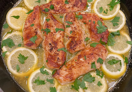 Pan-seared chicken fillets surrounded by sliced lemons in a skillet, garnished with parsley. The dish looks fresh, vibrant, and flavorful.