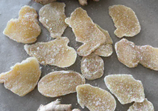 Close-up of golden-yellow, translucent, and irregularly shaped slices of candied ginger tossed in white sugar.
