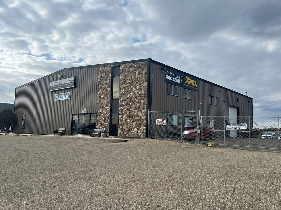 Auto center with stone accents and signs for rentals. A fenced area with no parking signs. Cloudy sky and a red car outside.