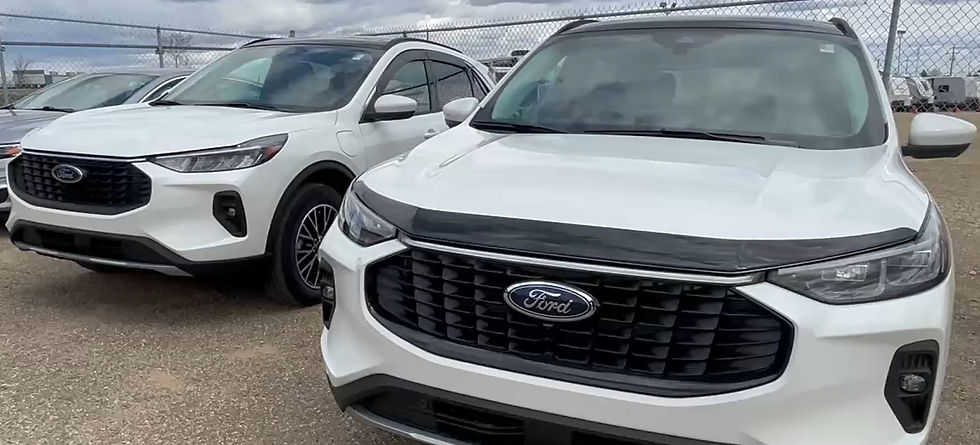Two white Ford SUVs parked next to each other on a gravel lot, with a chain-link fence and cloudy sky in the background.