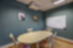 La salle de réunion est composée d'une table ovale avec 4 chaises autour, un tableau whiteboard dans le fond de la pièce, et 2 tableaux accrochés sur le mur.