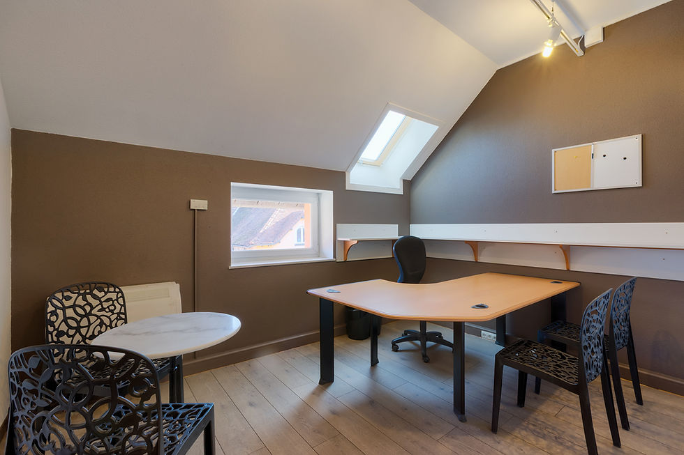 Un bureau avec des murs de couleur taupe et 2 fenêtres. Il y a un bureau principal et une petite table de réunion.
