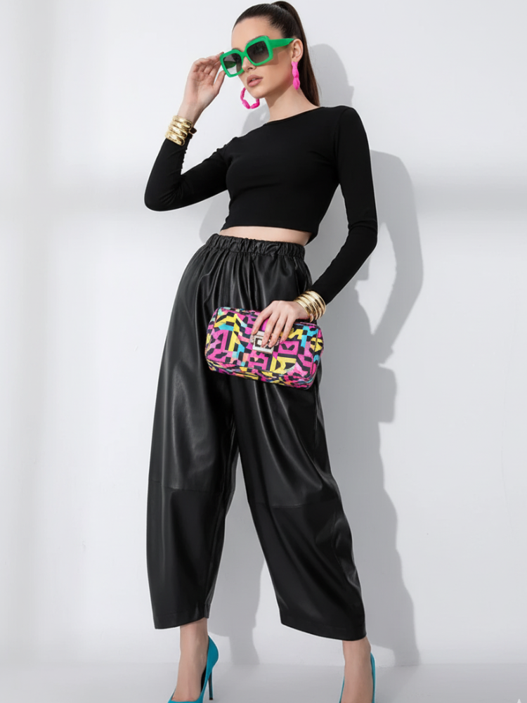 Woman wearing black top and pants, holding a colorful clutch in studio.
