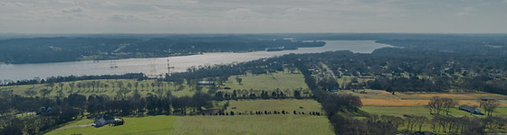 Vast fields, forestry, and a body of water, all with the horizon visible in the background during the day