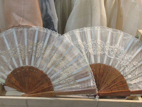 Two intricately designed lace Hand Fan Piña Fiber on displayed on a wooden stand. The delicate patterns stand out against a soft fabric backdrop.