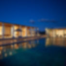Amanzoe, a luxurious villa at dusk, featuring a lit pool, striped loungers, and columns. Warm indoor lights create a serene, inviting atmosphere.