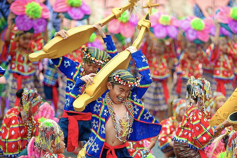 Kadayawan Festival of Davao City, Children in colorful traditional costumes joyfully dance, holding yellow instruments. Bright pink and green decorations fill the background.