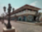 Looking at brown cobblestone street with old intricate street lanterns and an old white Spanish era building with arch windows.