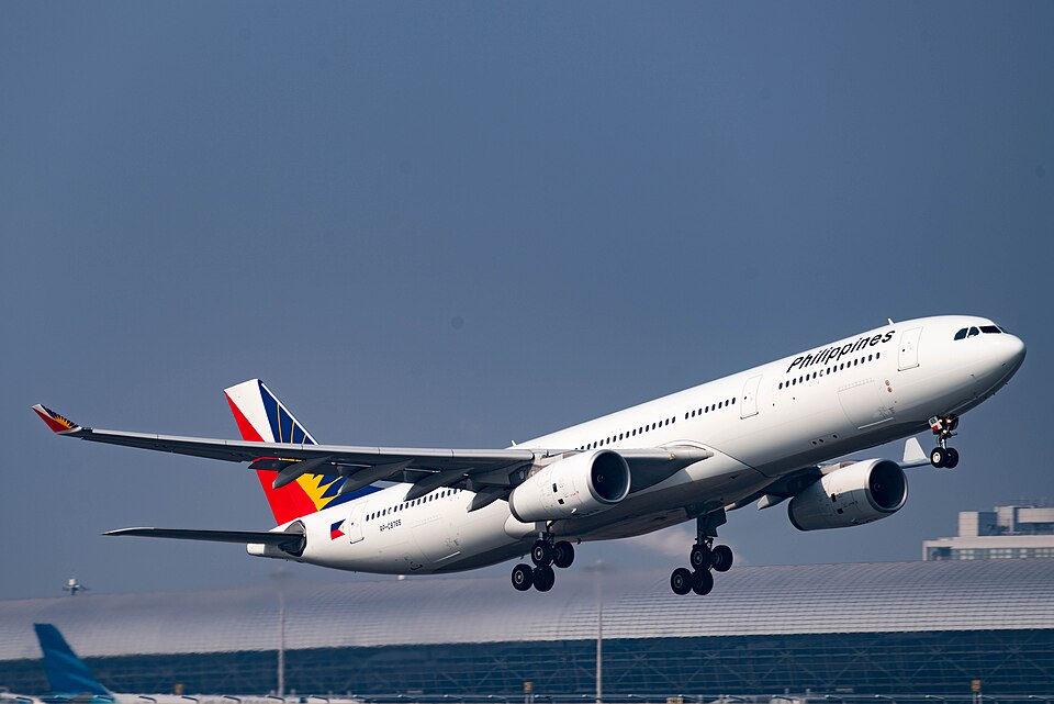 Philippine Airlines jet labeled Philippines lifts off above airport terminal under clear blue sky.