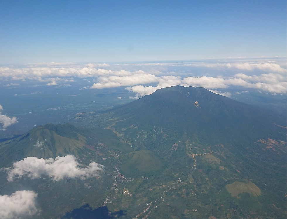 Aerial view of a green mountain landscape under a bright blue sky with scattered white clouds, showcasing expansive lush terrain.