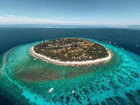 Balicasag Island an aerial view of a circular island surrounded by turquoise water, with scattered boats. Dense green foliage and a sandy beach line the island.
